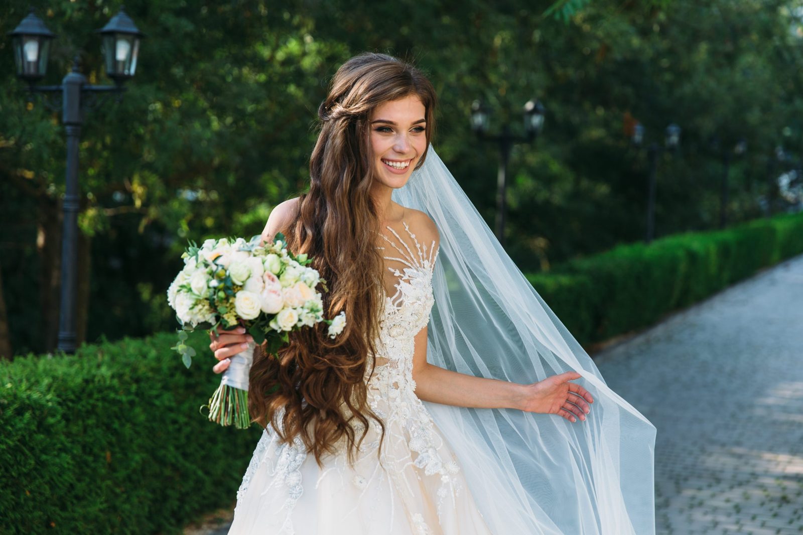 A smiling bride in a lace gown with a long veil