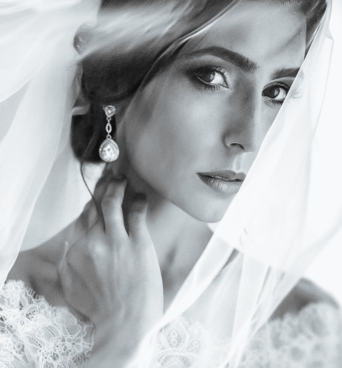 A bride in a lace gown and drop earrings, framed by her veil